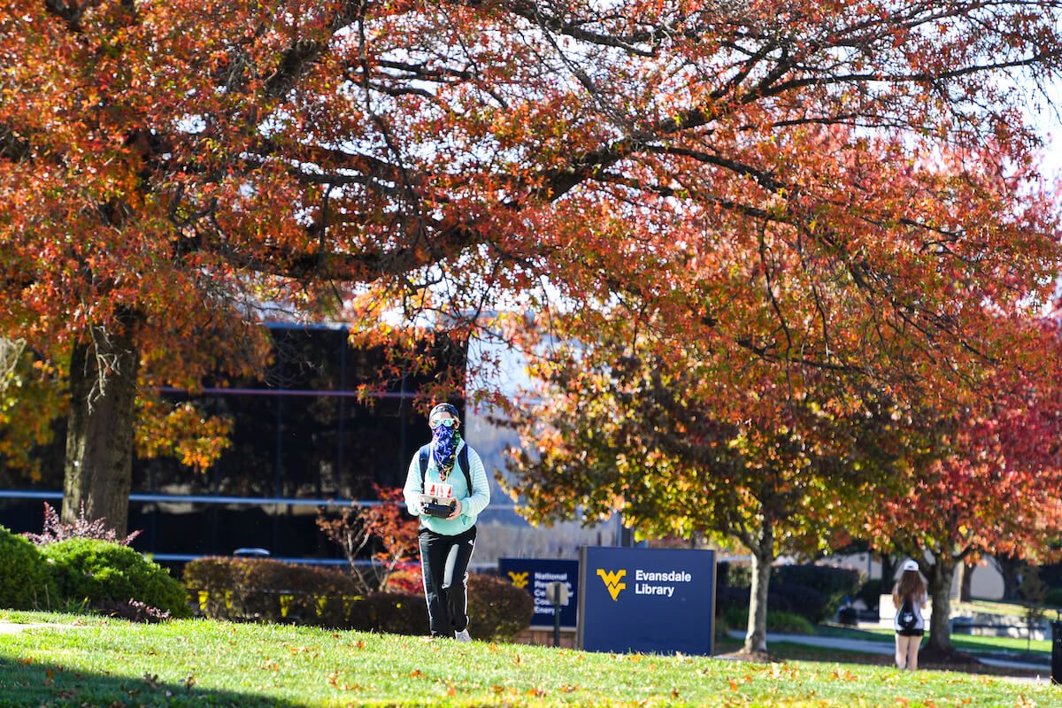 Student in mask walks by Evansdale Library