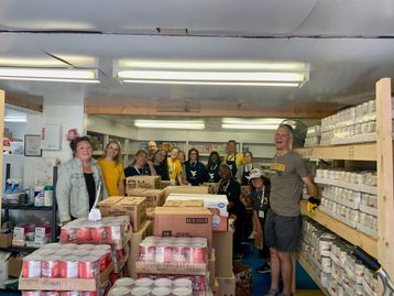 Canned food is stacked up on pallets and shelves in this photo which also includes more than half a dozen people working as volunteers