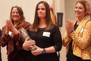 Image of WVU Faculty member Erin Goodykoontz as she accepts her award for teaching professor of the year. She is flanked by two female colleagues. 