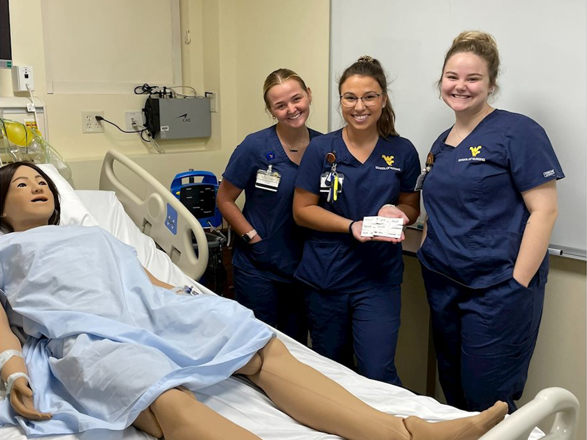 Three female nursing students and a patient dummy pose in a hospital room during a training exercise. 