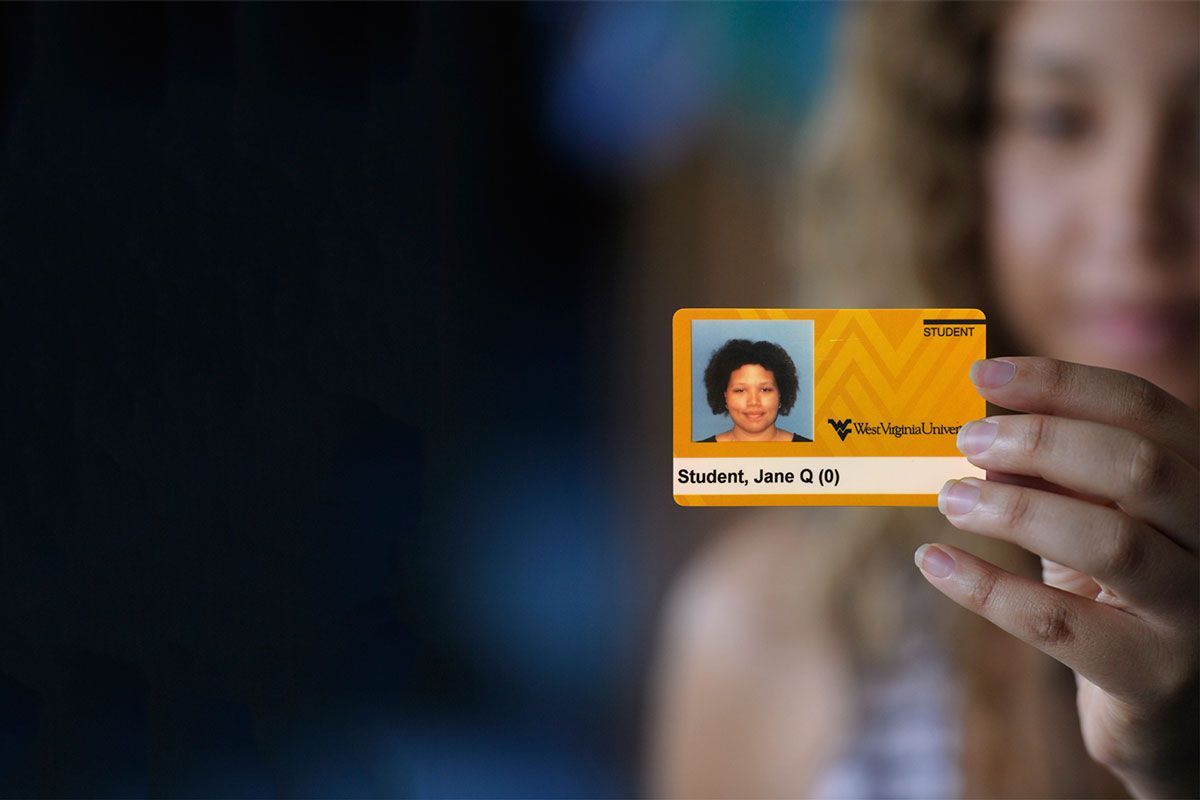 Image of a female WVU student holding up a mock WVU ID card. 