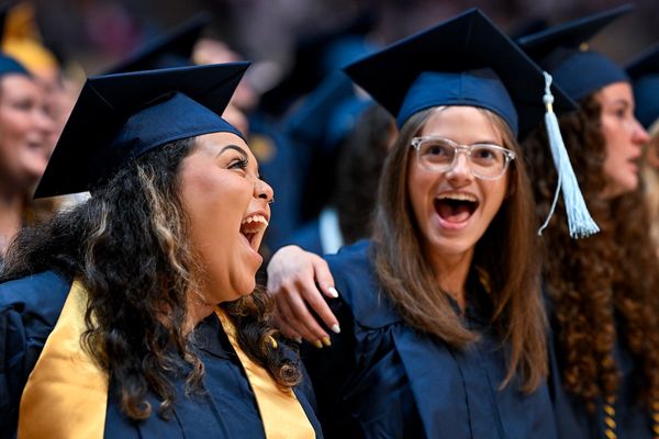 Two graduates sing 'Country Roads' to mark the end of a Commencement ceremony while wearing navy blue caps and gowns.