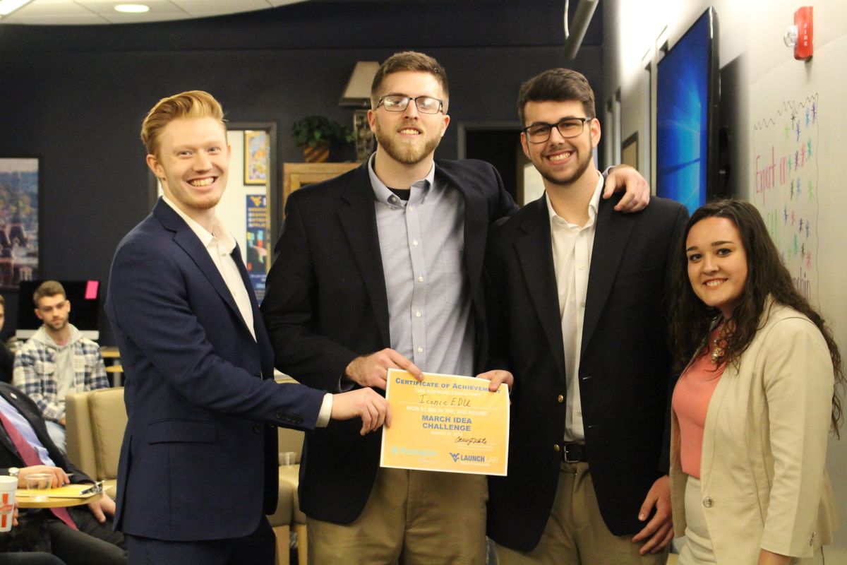Three male students and one female stand together with a winner's certificate