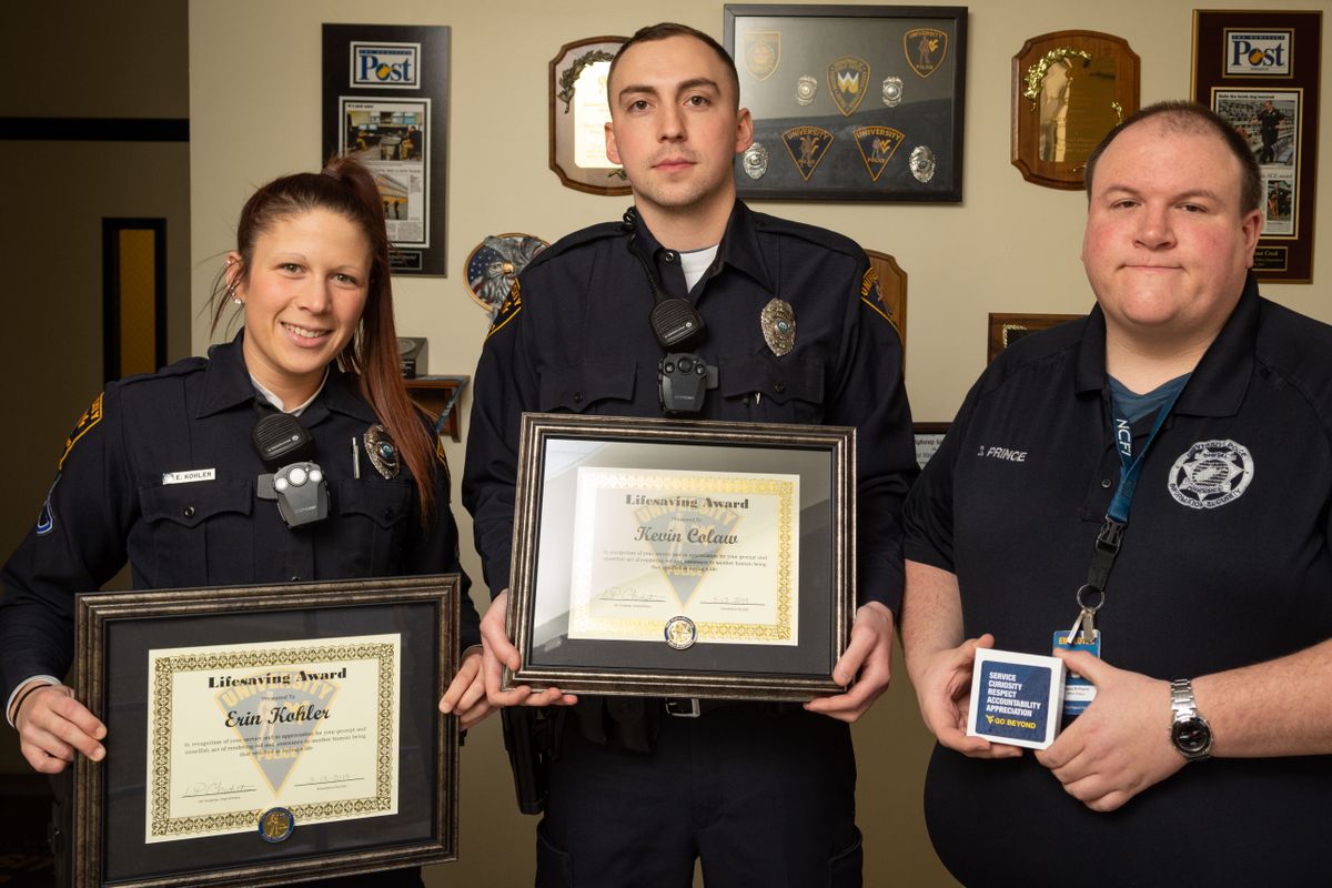 Two men and a woman in police uniforms hold plaques and an award