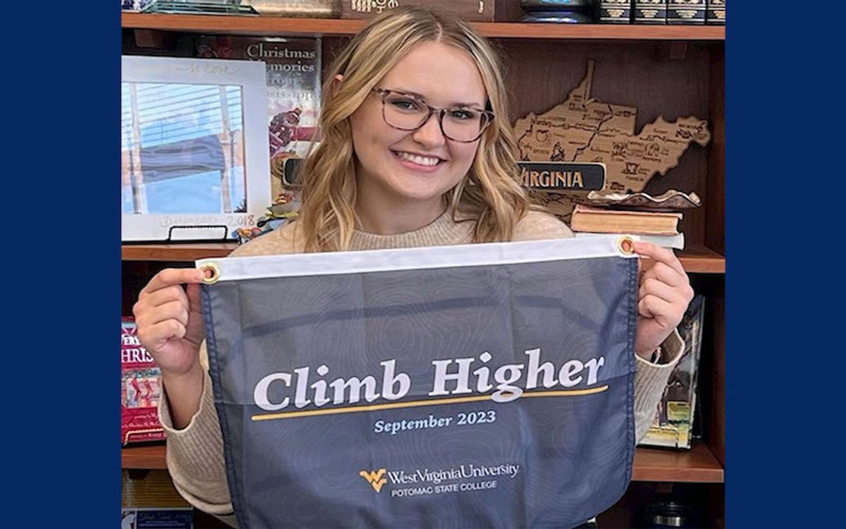 Girl with blonde hair wearing glasses holding Climb Higher sign