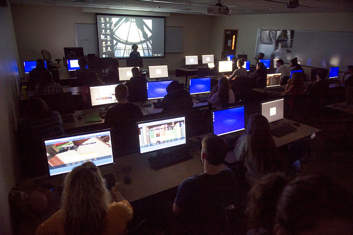 Photo of a darkened classroom with several computer screens, a larger screen at the front of the room