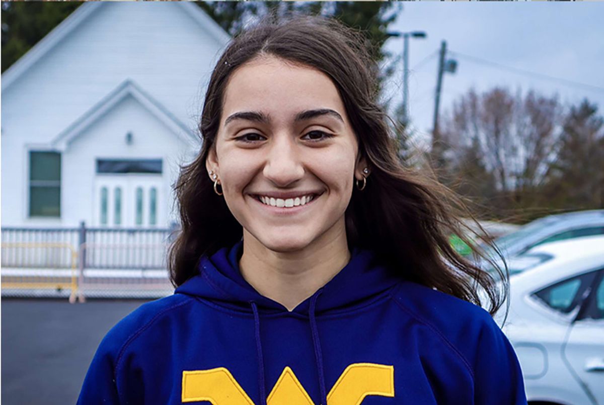 Headshot of WVU student Maria Vito. She is standing outside in a parking lot and she is wearing a blue WVU hoodie. She has long, brown hair. 